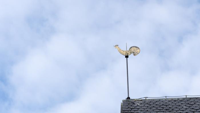 En kyrktupp på ett tak mot lätt molnig himmel.