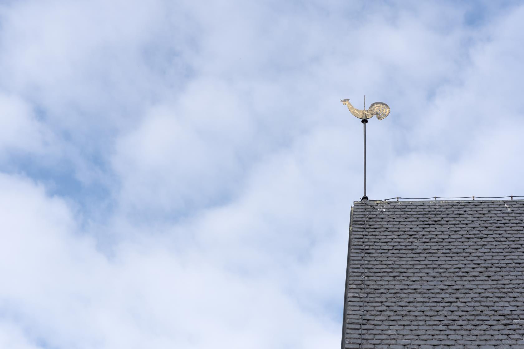 En kyrktupp på ett tak mot blå och molnig himmel.