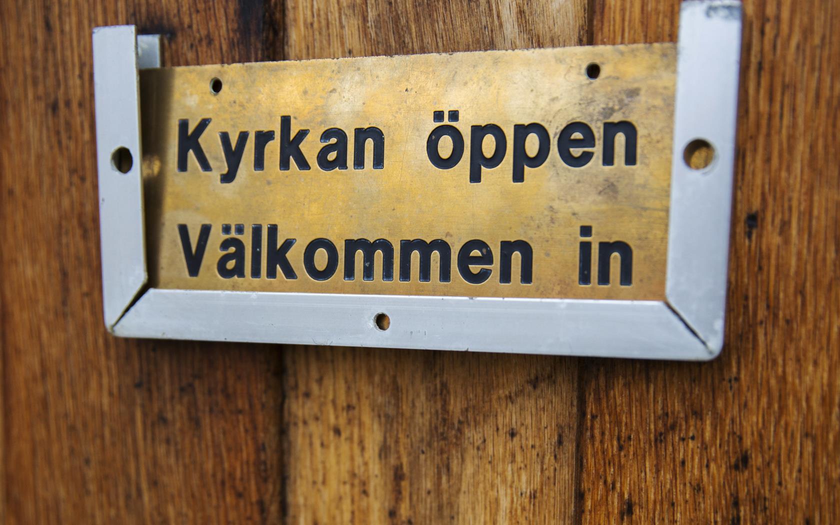 På en dörr sitter en skylt med texten Kyrkan öppen välkommen in.