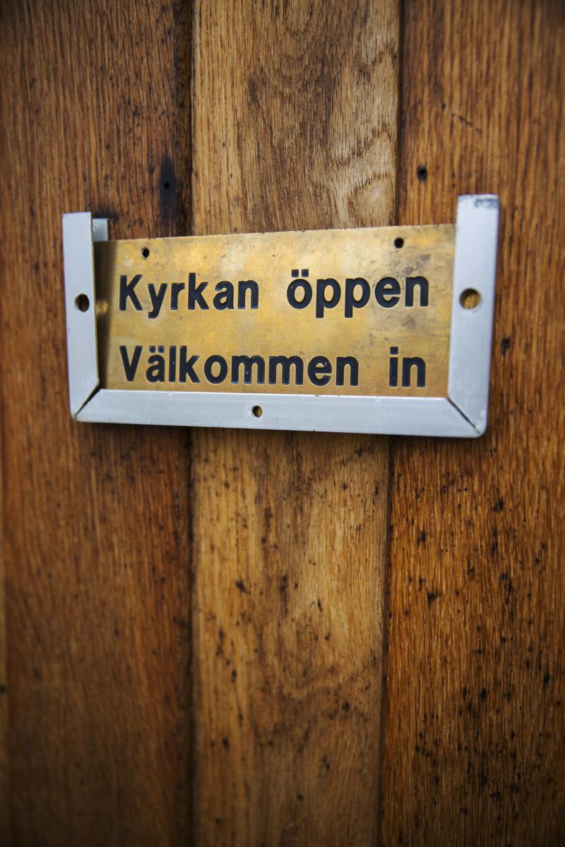 På en dörr sitter en skylt med texten Kyrkan öppen välkommen in.