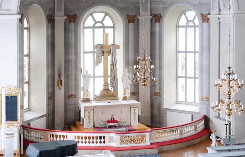 Ett stort kors och två statyer står på ett altare i en kyrka.