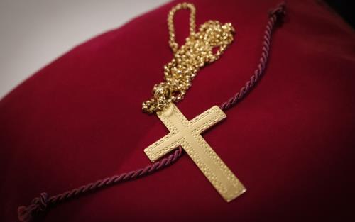 Ett halsband med ett guldigt kors ligger på en röd sammetskudde.