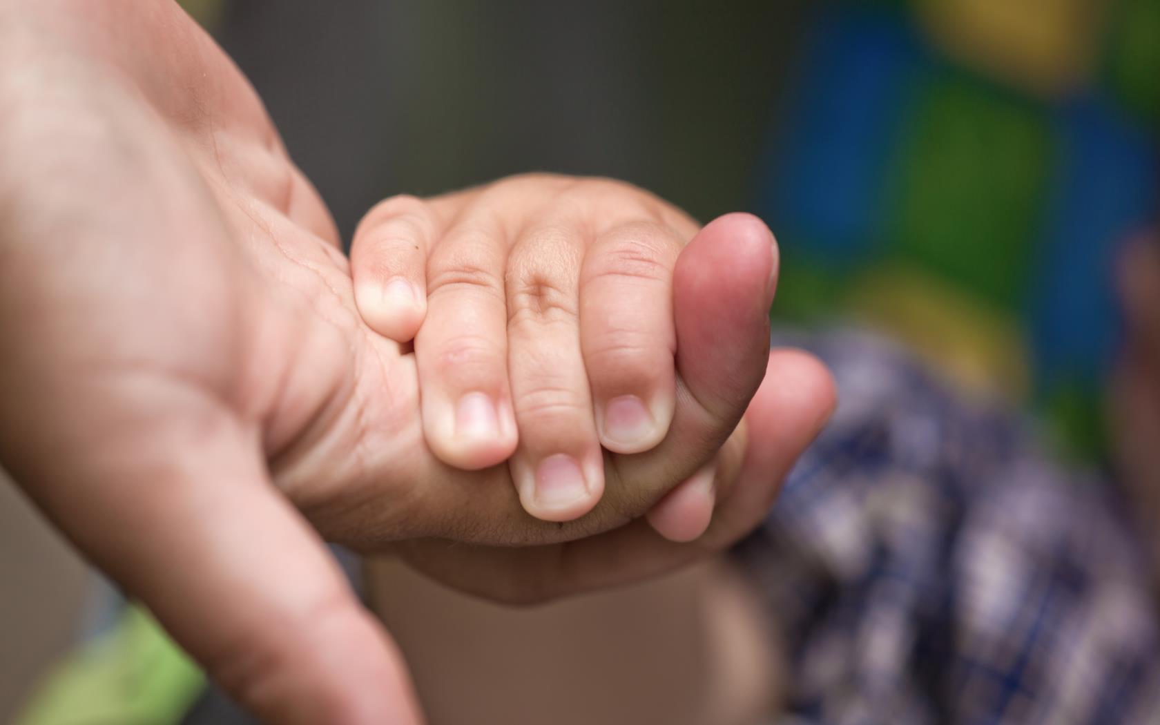 En liten barnhand håller om en vuxens finger.