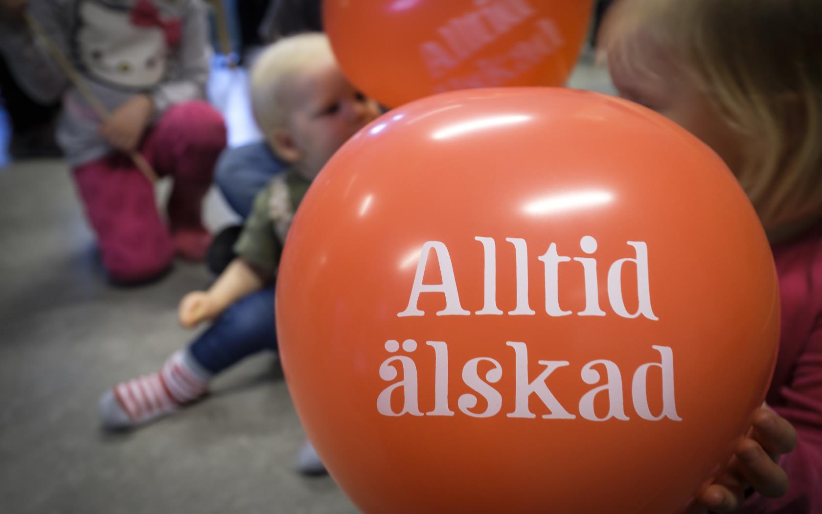 Några små barn med röda ballonger med texten Alltid älskad.