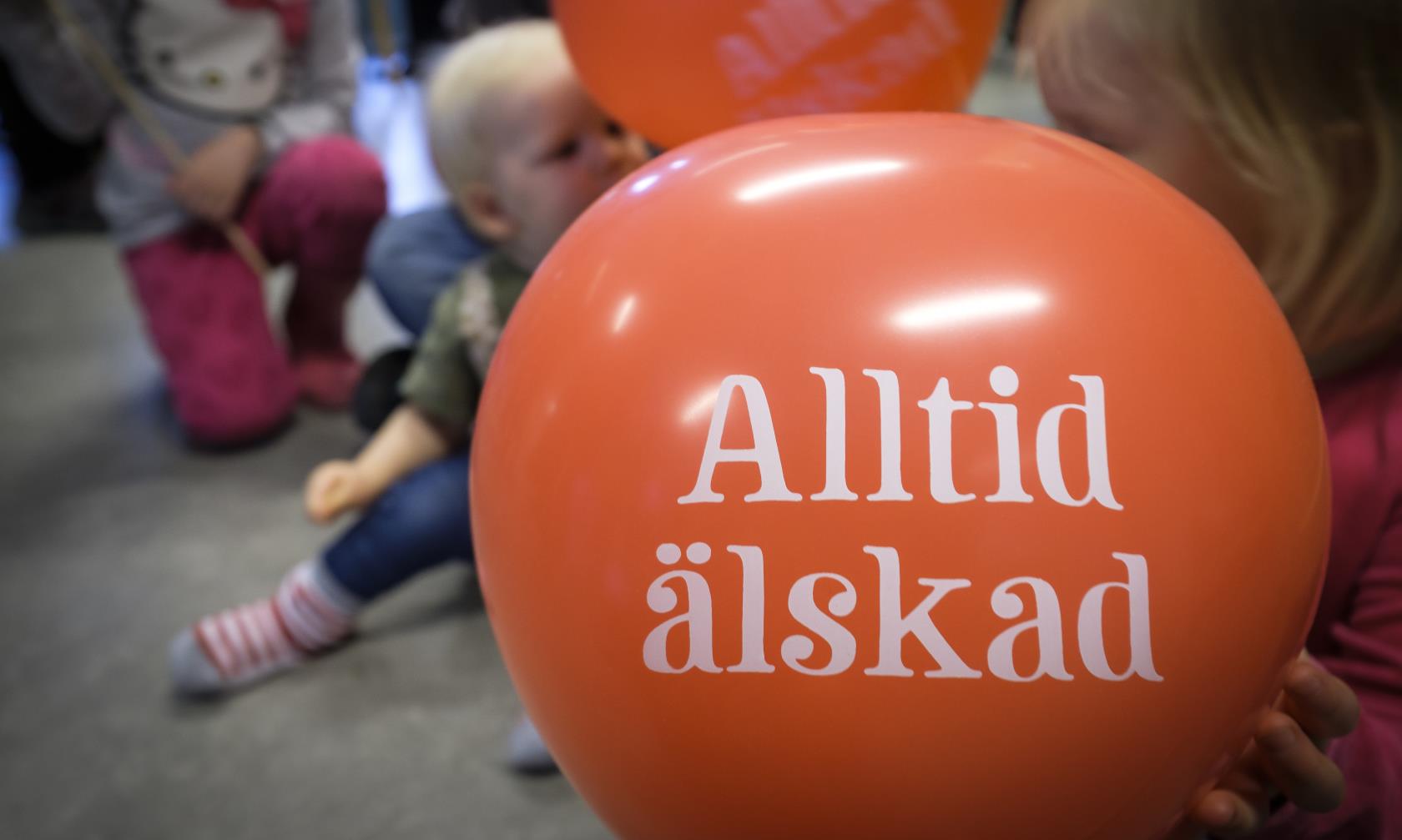 Några små barn med röda ballonger med texten Alltid älskad.