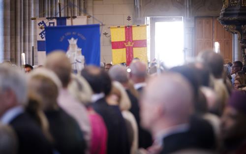 En stor församling i Uppsala domkyrka vänder sina ansikten mot den öppnade kyrkporten. En procession med banér kommer in.