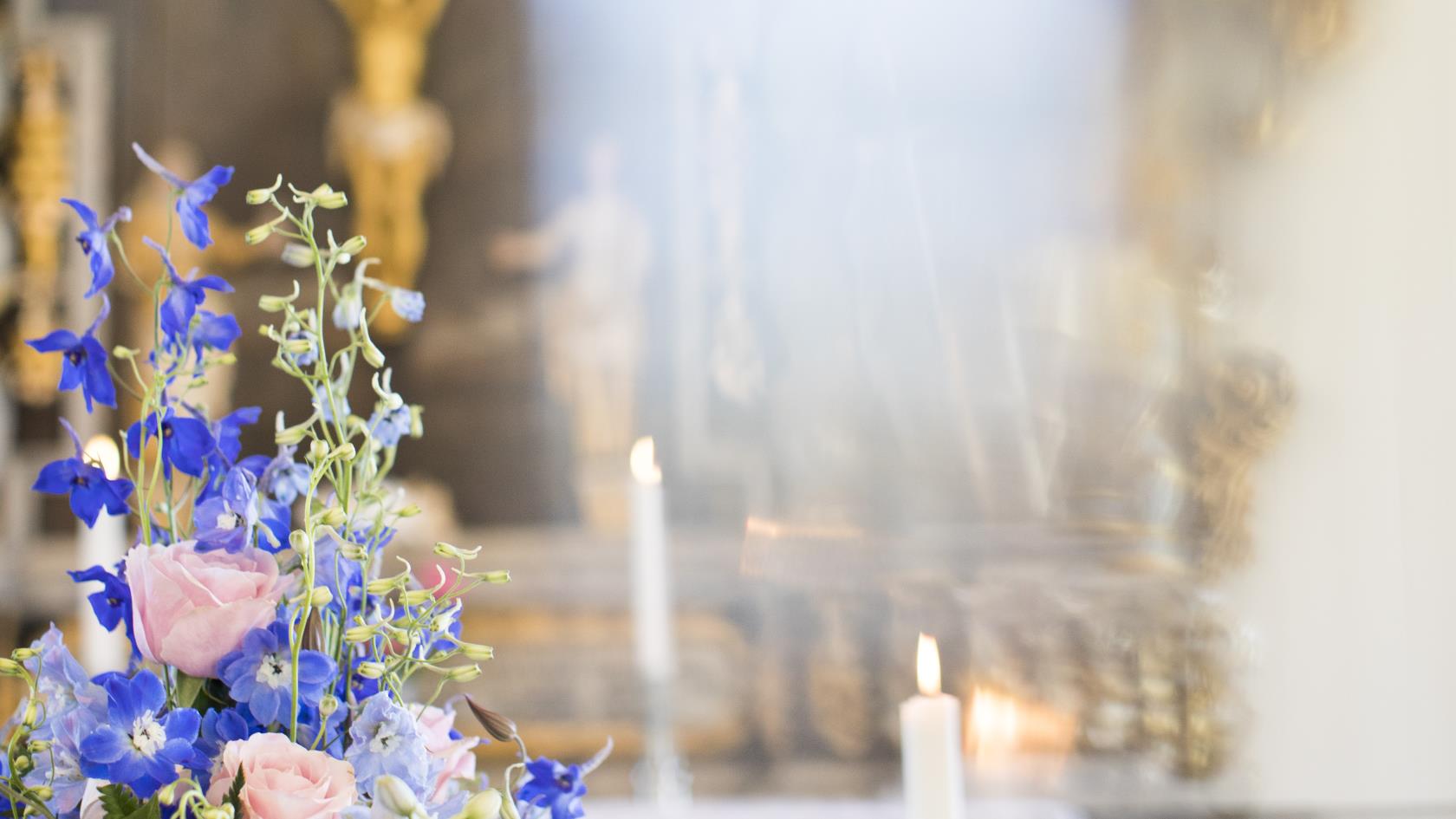 En begravningsbukett med skära och blå blommor ligger på en kista i en kyrka.