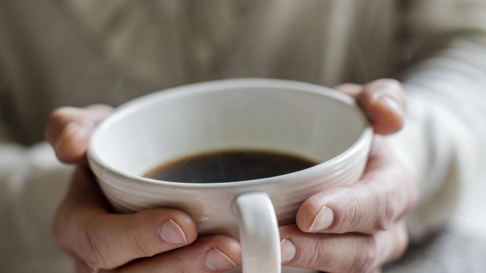 Någon håller händerna runt en kopp med kaffe.