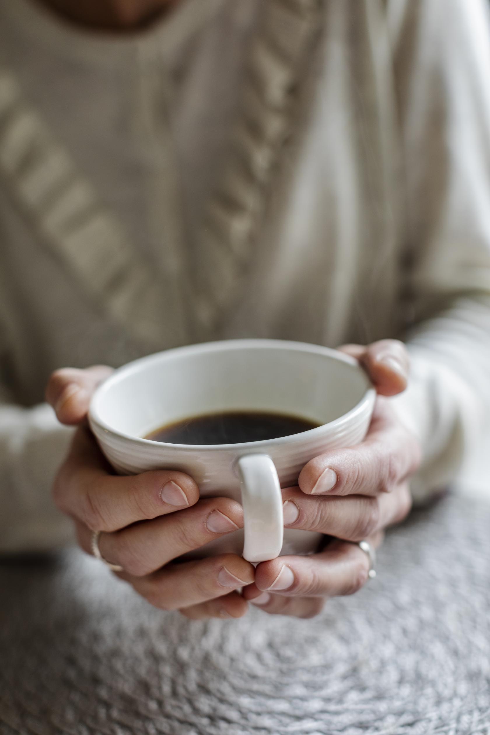 Någon håller händerna runt en kopp med kaffe.