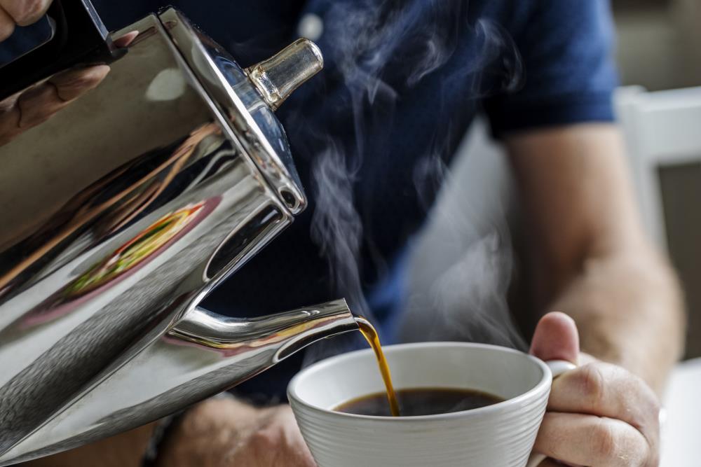 Någon häller upp kaffe till en man som sitter vid köksbordet.