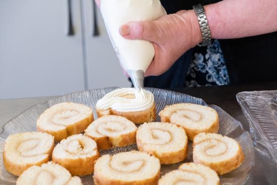 Någon spritsar på grädde på ett fat med rulltårtebitar.