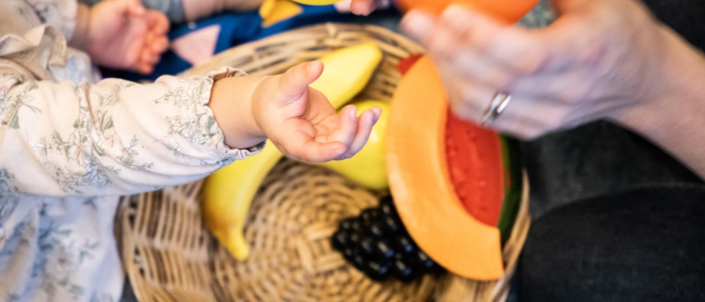 En bebis och en vuxen leker med plastfrukter.