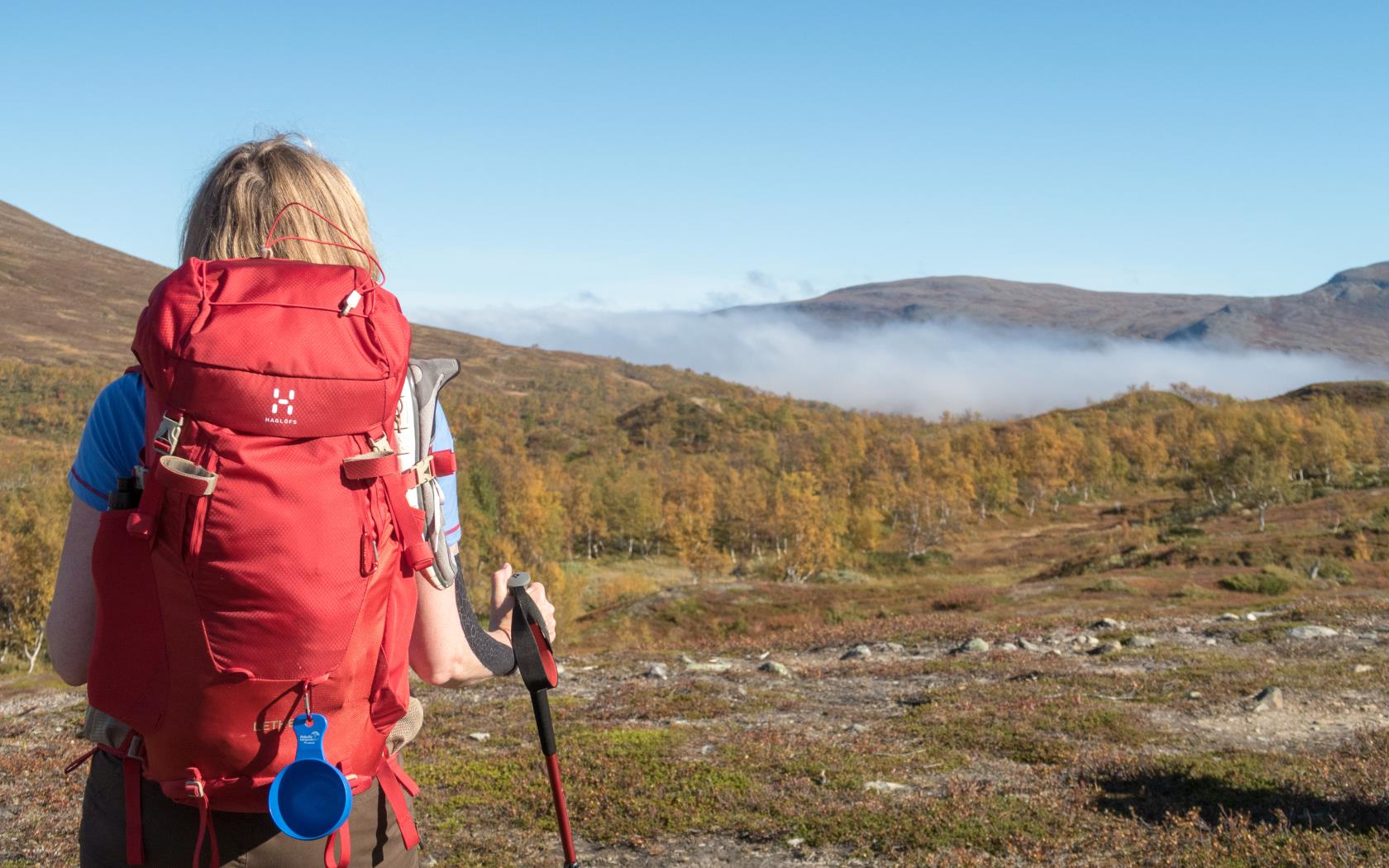 En kvinna med en stor röd ryggsäck sommarvandrar i fjällen.