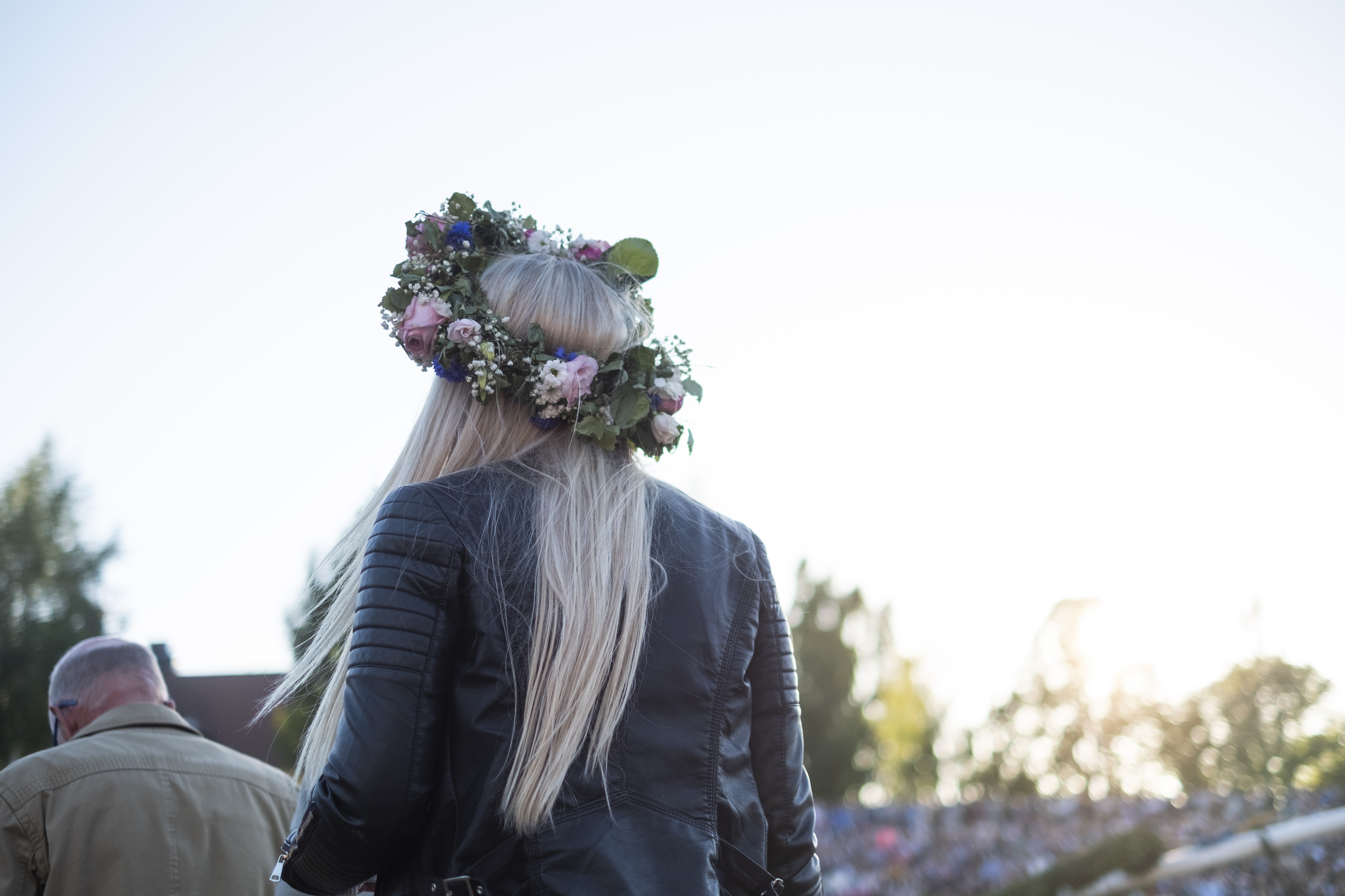 En blond tjej med läderjacka och en stor midsommarkrans på huvudet.