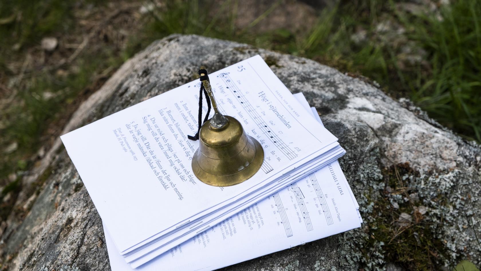 På en sten ligger notpapper. En ringklocka står ovanpå så de inte blåser iväg.