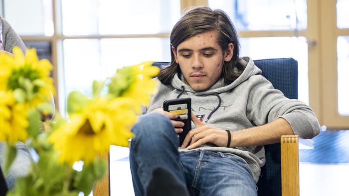 En ung kille sitter i en stol och håller på med mobiltelefonen.