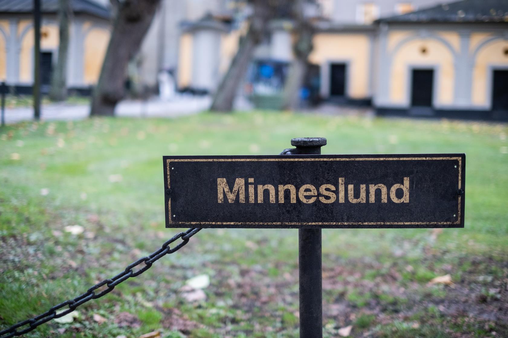 En svart skylt med texten Minneslund står utomhus.