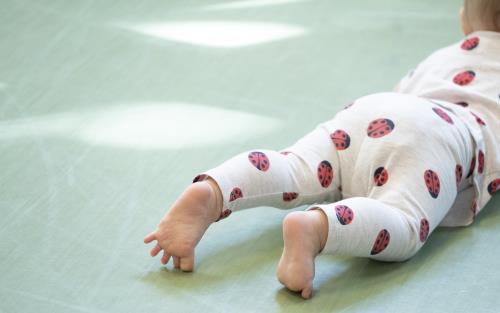 En bebis med nyckelpigor på kläderna ligger på mage på golvet.