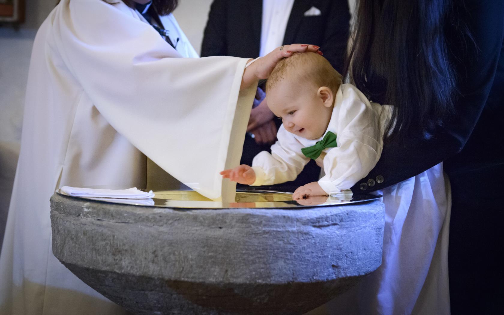 En liten bebis blir döpt. En kvinnlig präst håller sin hand på hans huvud.