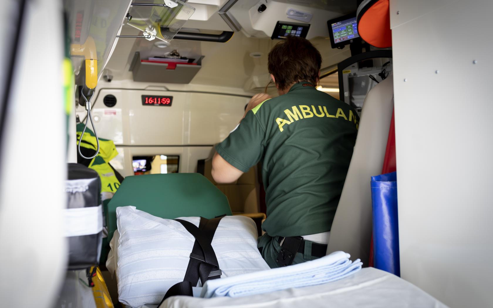 En ambulanssjukvårdare sitter bredvid den tomma britsen i ambulansen.