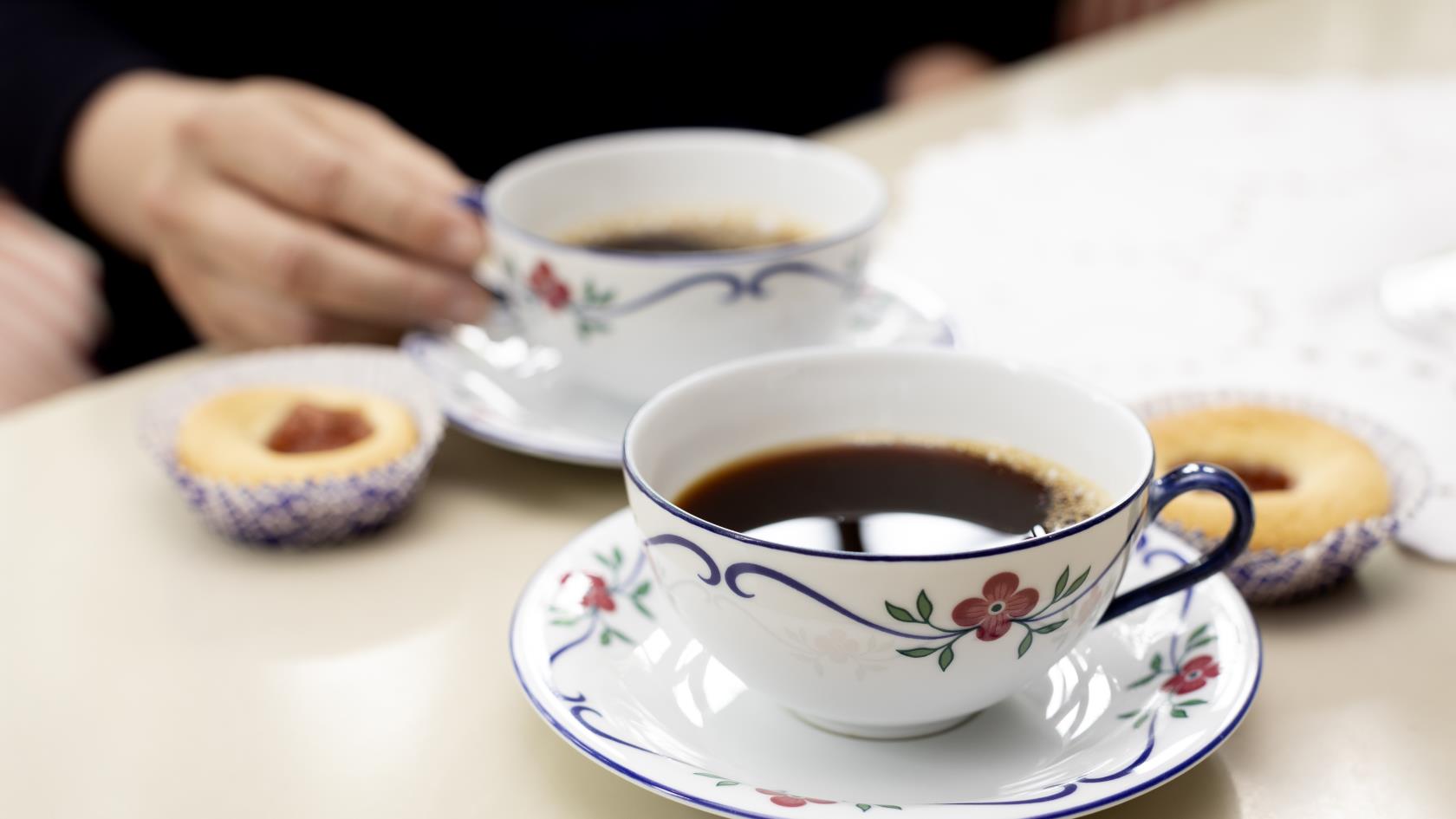 Närbild på två kaffekoppar på fat och hallongrottor.