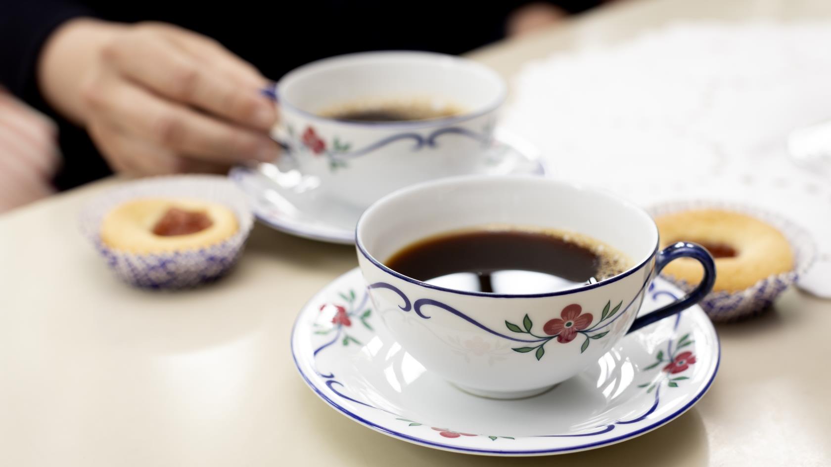 Närbild på två kaffekoppar på fat och hallongrottor.