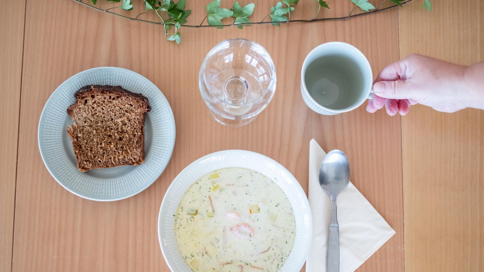 En skål soppa och en brödbit står framdukat på ett bord.