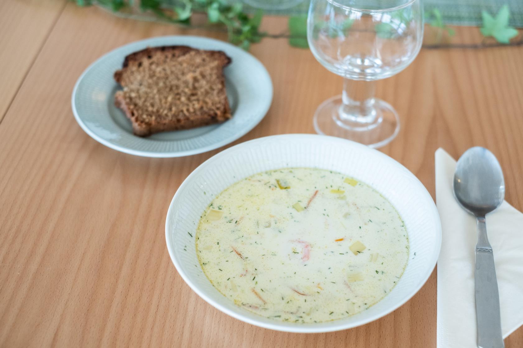 En skål soppa och en brödbit står framdukat på ett bord.