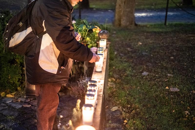 En person tänder ett gravljus som ställts uppe på ett stenstaket.