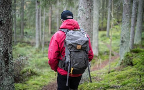 En man med ryggsäck går på en stig i skogen.