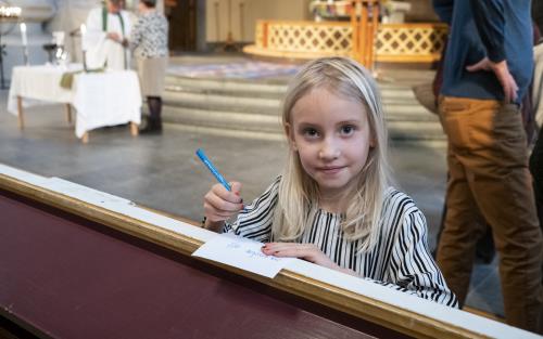 En flicka skriver något på ett papper framme i kyrkan.