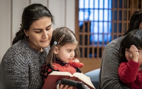 En kvinna sitter med sin dotter i knät och läser  bok.