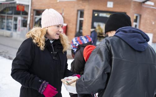 En kvinna står utomhus och delar ut mackor.