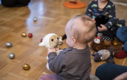 En bebis på golvet tittar på ett gosedjur som föreställer ett får.