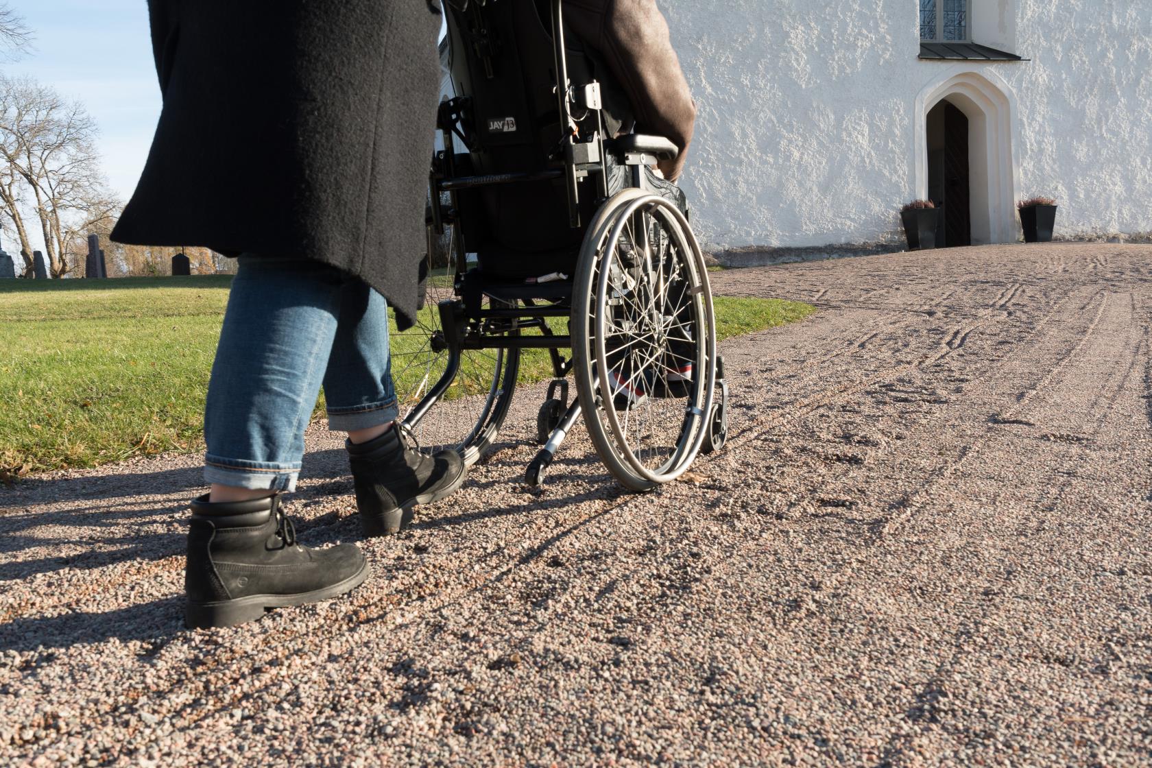 Någon kör en rullstolsburen person längs grusgången mot kyrkan.