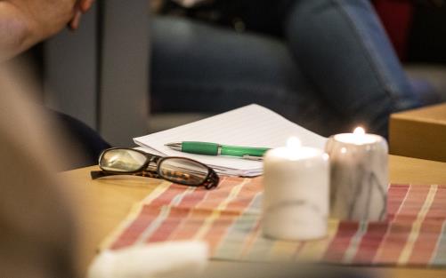 Ett par glasögon, papper och penna ligger på bordet bredvid några stearinljus.