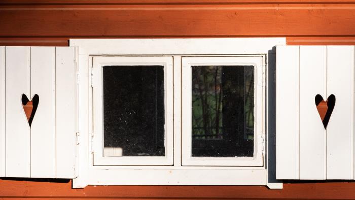 Ett fönster på ett falurött hur har fönsterluckor med urfrästa hjärtan i.