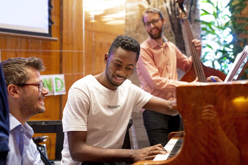 Tre män spelar piano och kontrabas tillsammans.