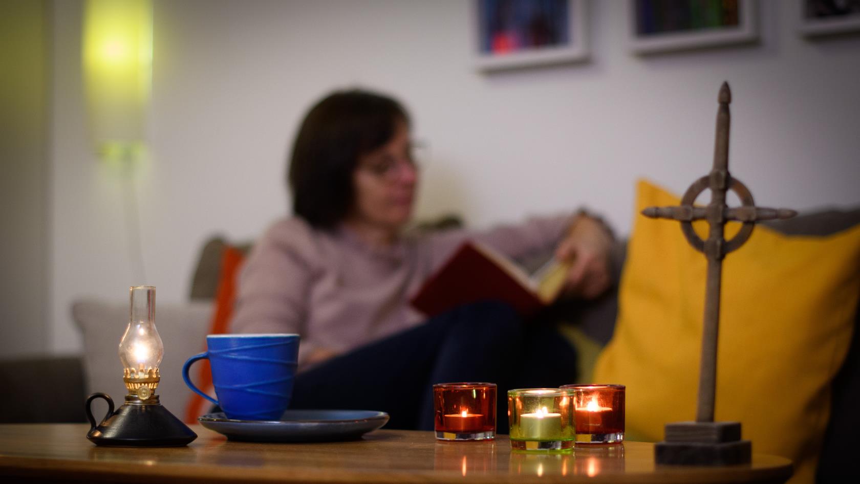 En kvinna läser hemma i soffan. På soffbordet framför henne står tända ljus och ett kors.