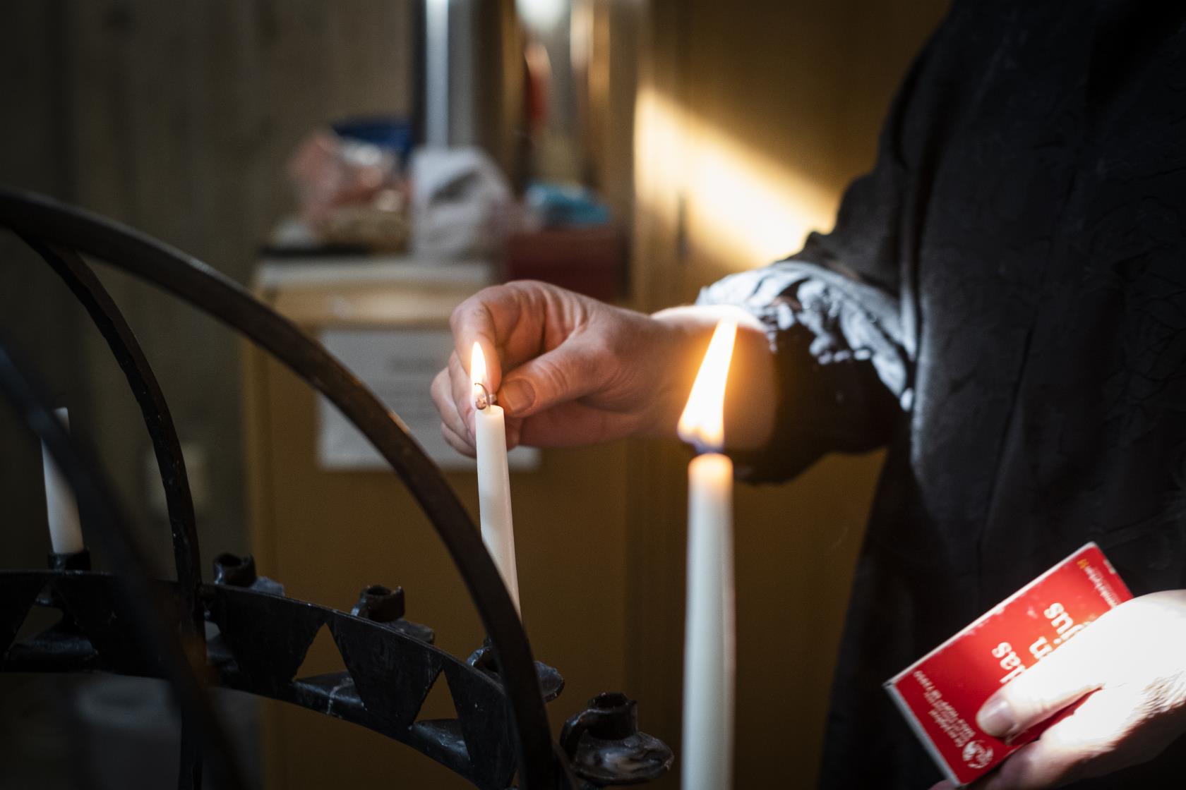 Någon tänder ljus i en svart ljusbärare.