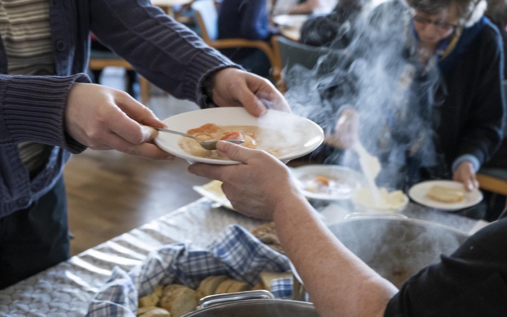 En person serverar soppa och bröd till äldre.