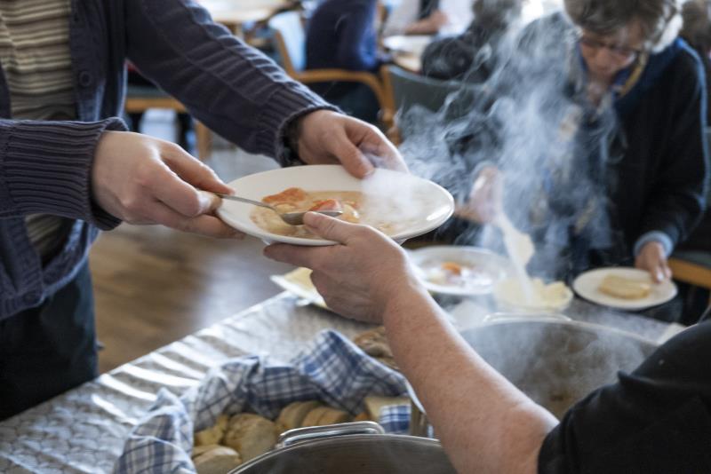 En person serverar soppa och bröd till äldre.