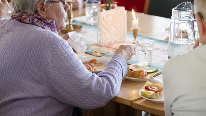 En äldre kvinna sitter och äter tillsammans med andra.