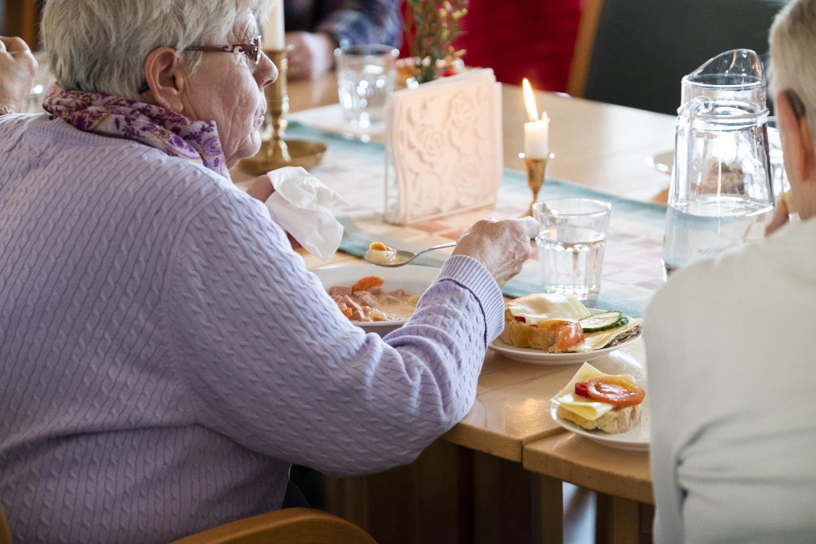 En äldre kvinna sitter och äter tillsammans med andra.