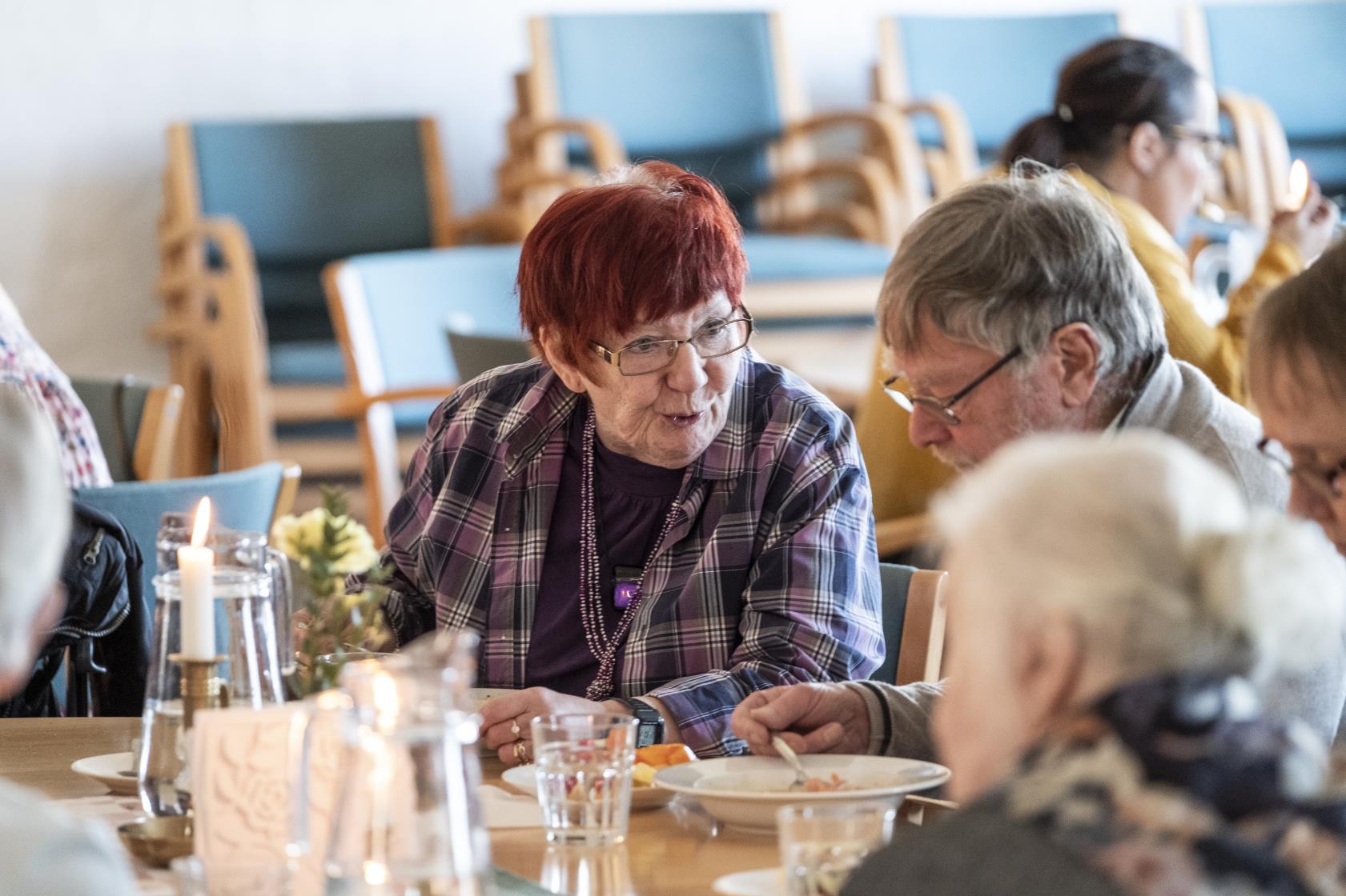 Några äldre personer sitter vid ett bord och äter soppa och samtalar.