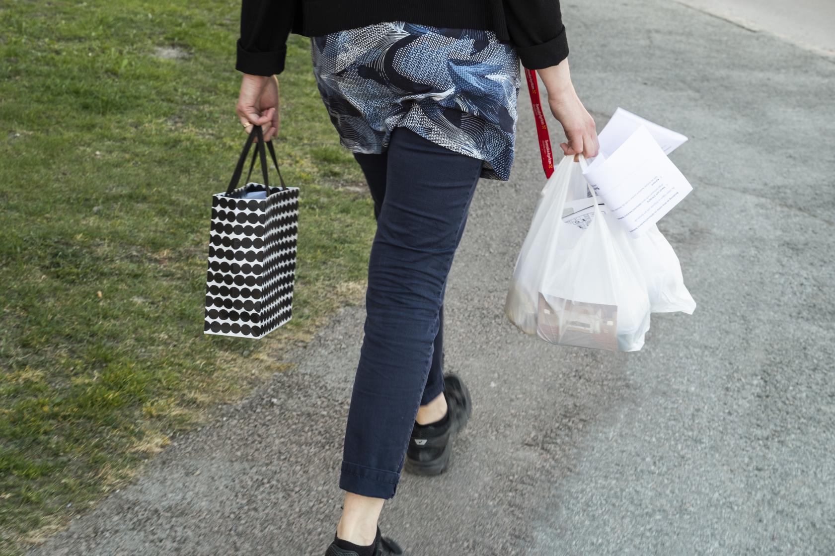 En person går med en prickig påse i ena handen och en fylld plastkasse i den andra.