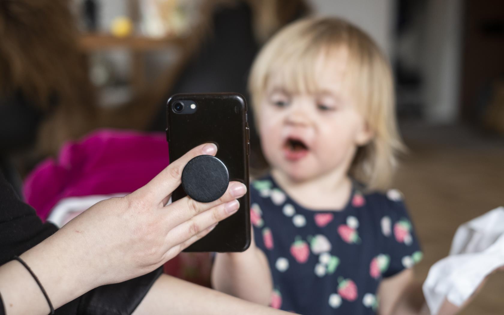 Någon håller upp en mobiletelefon mot en liten flicka.