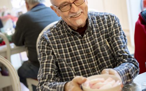 En äldre man sitter vid ett bord. Han håller en skål med skumtomtar i händerna.