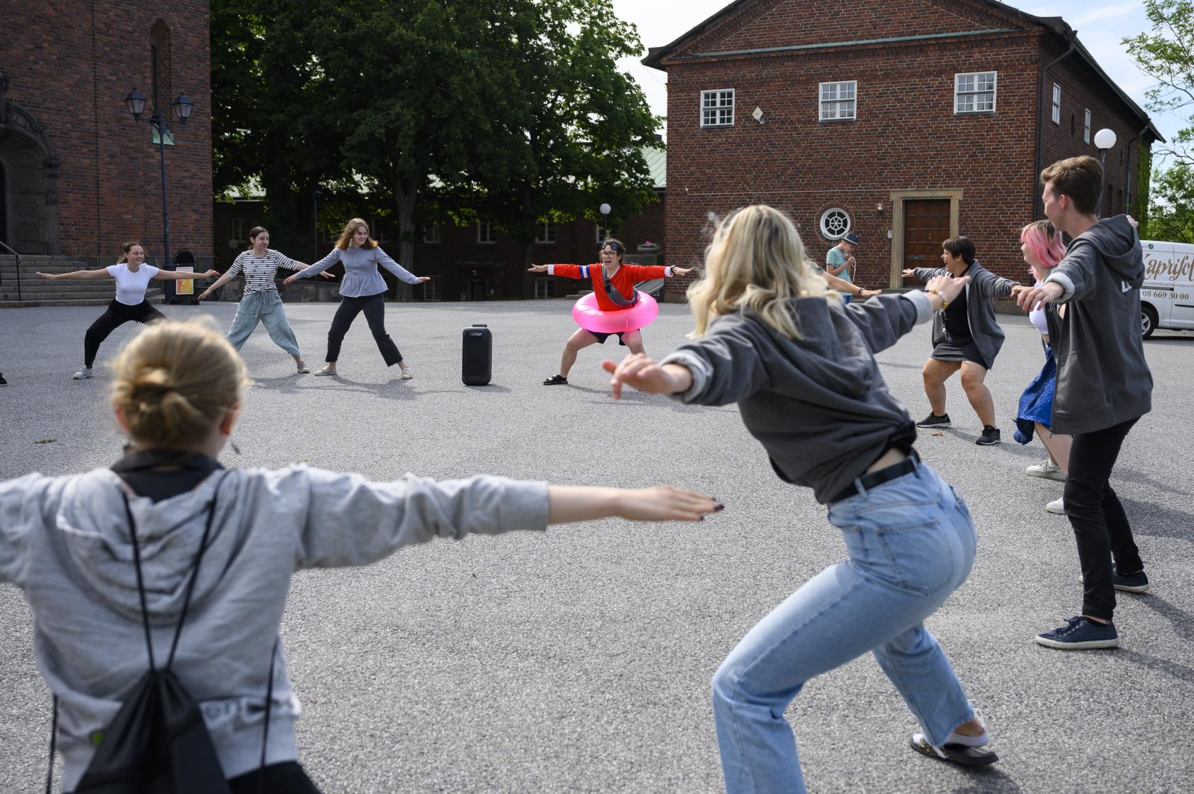 Några ungdomar och en ledare står i ring utomhus med armarna utsträckta och böjda knän.