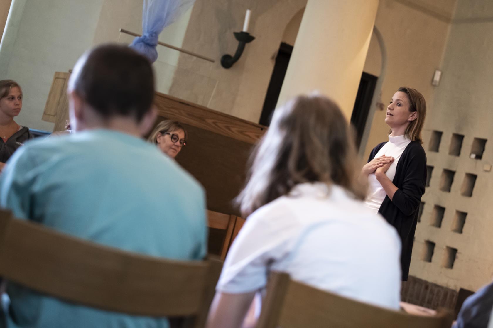 En kvinna står upp i en kyrka. Hon håller händerna mot bröstet.